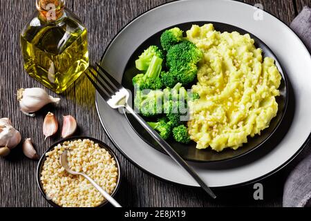 Brokkoli Kartoffelpüree mit gehackten Mandeln bestreut serviert mit gedünsteten Brokkoli blüsst auf einem schwarzen Teller auf einem dunklen Holz Tabelle Stockfoto