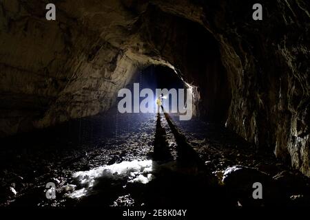 11 Jahre alter Junge in einer Höhle stehend, beleuchtet BU eine Hintergrundbeleuchtung, geschmolzene Stalagmiten aus Eis in der Front, Slowenien Stockfoto