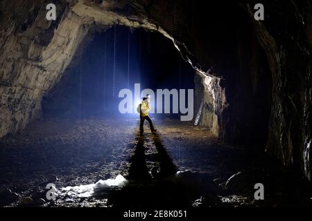 Der 11-jährige Junge steht in einer Höhle, beleuchtet von einer Hintergrundbeleuchtung, geschmolzene Stalagmiten aus Eis im vorderen Teil Sloweniens Stockfoto