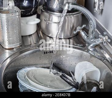 Wasserstrahl fließt aus dem Wasserhahn auf schmutziges Geschirr Spülbecken in der Küche Stockfoto