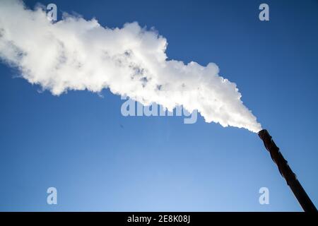 Eine lange Wolke aus weißem Rauch, die aus einem metallischen Kamin gegen einen tiefblauen Himmel entweicht. Foto Bo Arrhed Stockfoto