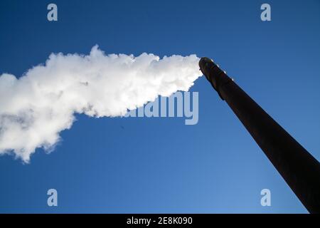 Eine lange Wolke aus weißem Rauch, die aus einem metallischen Kamin gegen einen tiefblauen Himmel entweicht. Foto Bo Arrhed Stockfoto