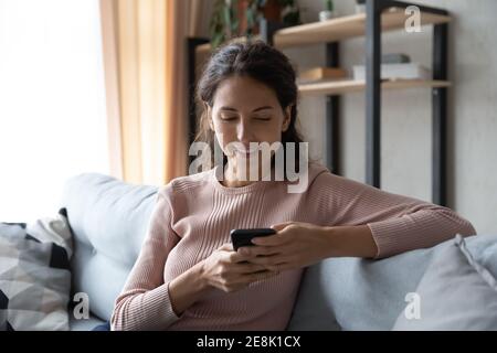 Entspannte junge Frau mit Smartphone auf dem Sofa sitzen. Stockfoto