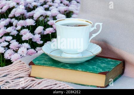 Eine Tasse Tee steht auf einem alten Buch. Im Hintergrund sind rosa Chrysantheme Blüten Stockfoto