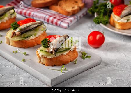 Geräuchertes Sprotte Sandwich - Fisch, frische Gurken und Tomaten. Sproat Sandwiches auf gerösteten Brotscheiben Stockfoto