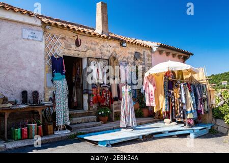 Farbenfrohe Ausstellung von Sommerkleidung für Frauen auf einer Terrasse vor einem Laden in einem rustikalen Gebäude an der Via Torres in San Pantaleo, Gallura, Sardinien. Stockfoto