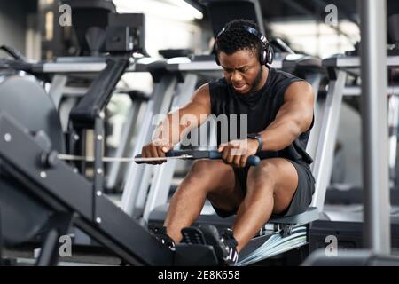 Motivierter schwarzer Sportler beim Training auf dem Rudergerät Stockfoto