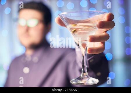 Kaukasischer Mann hält Glas martini mit Olive auf dem Hintergrund Stockfoto