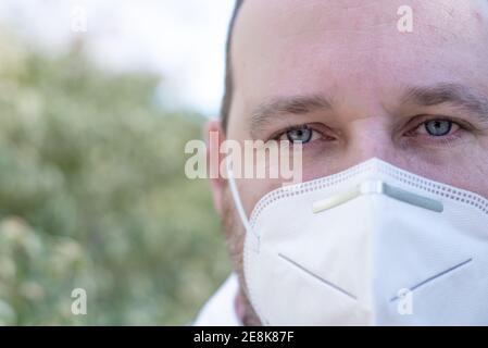 Schöner junger Europäer in Winterkleidung auf der Straße mit einer medizinischen Maske. Nahaufnahme eines 35-jährigen Mannes auf einem Atemschutzgerät, um sich zu schützen Stockfoto