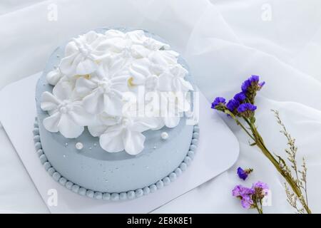 Pastellblau Kokosnusskuchen mit weißen Blumen aus frischer Sahne auf weißem Tuch dekoriert. Hausgemachtes und minimales Kuchenkonzept Stockfoto