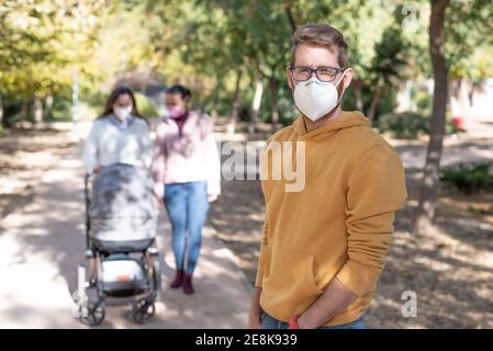 Junger Mann mit Maske und zwei Frauen mit Maske gehen ihr Baby. Zeiten covid 19 Pandemie. Aktives Quarantäneleben im Corona-Ausbruch Stockfoto