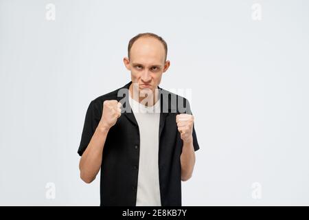 Sich verteidigend steht in einer Haltung mit fertigen Fäusten junger Glatze Mann in schwarzem Hemd mit weißem T-Shirt unter. Wütend jungen erwachsenen Mann zeigt er ist Stockfoto