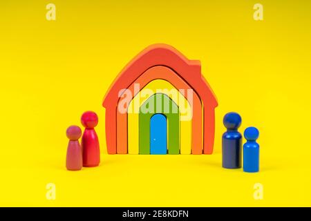 Holzfiguren, Miniaturmenschen, die vor dem Haus auf gelbem Hintergrund stehen. Scheidung, Konflikt zwischen Eltern Stockfoto