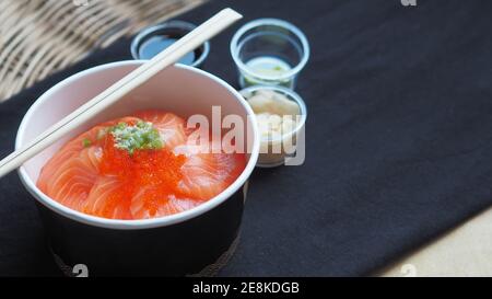 Draufsicht und Fokus auf Lachs mit japanischem Reis oder Lachs Ikura Don in Papierform von Delivery Restaurant auf Schwarze Tischdecken Stockfoto
