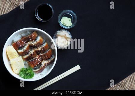 Draufsicht und Fokus auf Unadon oder unagi Donburi oder Aal Schüssel ist ein Gericht mit Ursprung in Japan auf schwarzem Hintergrund. Stockfoto