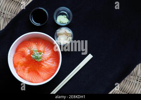 Draufsicht und Fokus auf Lachs mit japanischem Reis oder Lachs Ikura Don in Papierform von Delivery Restaurant auf Schwarze Tischdecken Stockfoto