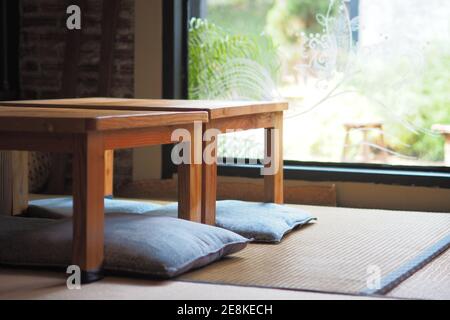 Zimmerdekoration im japanischen Stil mit Holztischen und Sitzkissen, grüner Garten im Hintergrund. Stockfoto