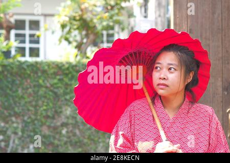 Weicher Fokus auf traditionelle japanische Yukata junge Mädchen mit rotem Regenschirm im Garten, asiatische Mädchen in Yukata mit Regenschirm, japanische Tradition Konzept Stockfoto