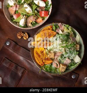 Lachssalate mit Mozzarella-Käse und gegrillten Obstscheiben stehen auf einem mit einem Lederlappen bedeckten Tisch. Restaurantkonzept. Quadratisch beschnitten Stockfoto