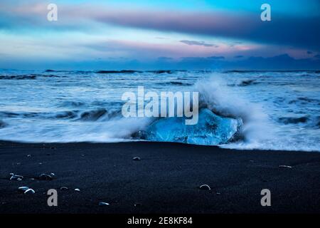 Schöne Landschaft von einem schwarzen vulkanischen Sandstrand mit Eisbergen. Wellen gegen einen großen Eisblock an der Küste. Erstaunliche Natur von Vatnajokull Stockfoto