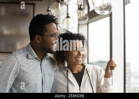 Junge schwarze Ehegatten stehen an Panoramafenster halten Tasten träumen Stockfoto