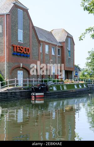 Ein Kanalboot mit Topfblumen auf der Oberseite, das an der Seite des Grand Union Kanals bei Rickmansworth neben Tesco Superstore festgemacht ist. Stockfoto