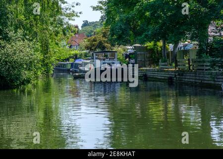 Kanalboote liegen auf dem Schleppweg am Grand Union Canal, Rickmansworth, England. Bäume & Wohnhäuser. Stockfoto