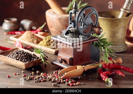 Alte Pfeffermühle mit Küchengeräten, Gewürze und Rosmarin auf einen hölzernen Tisch. Stockfoto