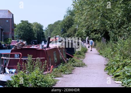 Mann mit Kleinkoffer geht an sonnigen Sommertagen entlang des Canals der Grand Union, Rickmansworth. Tesco Superstore am linken Ufer. Stockfoto