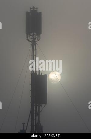Kommunikationsturm auf einem Gebäude mit 4G 5G Antenne bei Sonnenaufgang im Nebel. Stockfoto