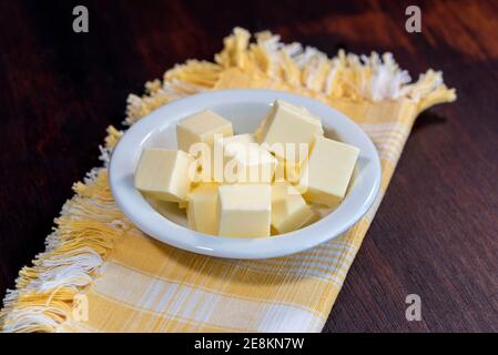 Schüssel mit Stücken frischer Butter auf einer gelben Serviette Auf dem Holztisch