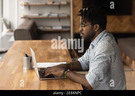 Fokussierter schwarzer junger Mann, der auf dem Laptop auf dem Bildschirm tippt Stockfoto