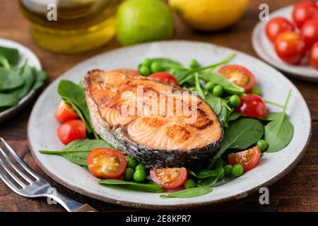 Geröstetes Lachssteak mit Babyspinat und Kirschtomaten auf einem Teller. Gesunde Mahlzeit Stockfoto
