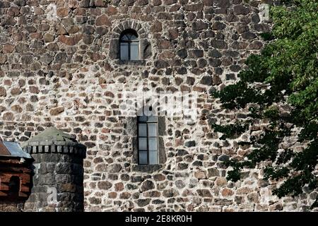 Alte Steinmauer mit kleinen Fenstern und einem Turm. Stockfoto