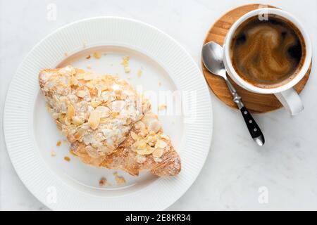 Kaffeetasse und Mandelcroissant auf weißem Marmortisch. Kaffeepause, Frühstück Essen am Morgen Stockfoto