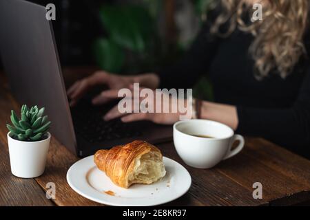 Unkenntlich Frau Freiberuflerin arbeitet am Laptop im Café. Croissant und eine Tasse schwarzen Kaffee auf der Seite. Geschäftsfrau Stockfoto