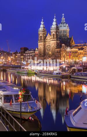 Amsterdam, Niederlande Blick ins Stadtzentrum mit Flussbooten und der Basilika St. Nikolaus bei Nacht. Stockfoto