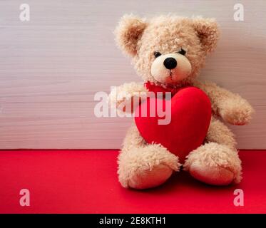 Valentinstag. Teddybär hält ein großes Herz sitzt auf rotem Boden, Holzwand Hintergrund, Kopierraum, valentines Karte Vorlage Stockfoto