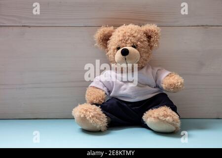 Teddybär trägt blaue Hose und weißes T-Shirt sitzt in einem leeren Raum, Kid Alone Konzept Stockfoto