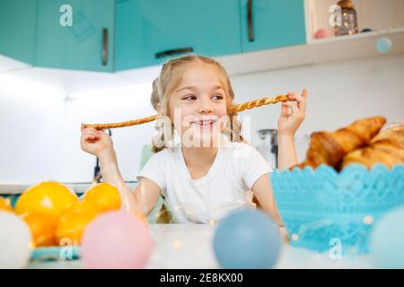 Porträt eines kleinen Mädchens 7 Jahre alt sitzt in der Küche und spielt mit Brotstangen. Kind hat Frühstück in der Küche Stockfoto