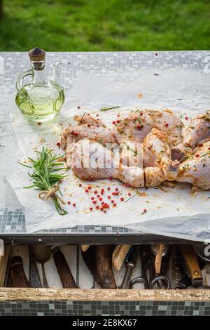 Würzen von Hähnchenbeinen zum Grillen mit Pfeffer, Salz und Oliven im Garten Stockfoto