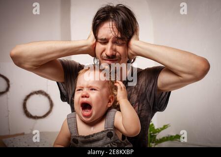 Das Kind schreit hysterisch. Ein müder Vater will das Baby nicht hören. Der Elternteil ist irritiert, müde, will eine Pause von seiner Tochter machen Stockfoto