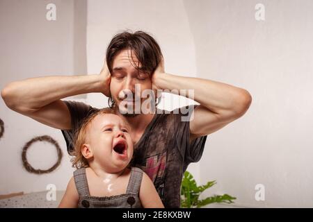 Das Kind schreit hysterisch. Ein müder Vater will das Baby nicht hören. Der Elternteil ist irritiert, müde, will eine Pause von seiner Tochter machen Stockfoto