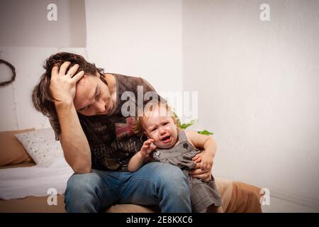 Das Kind schreit hysterisch. Ein müder Vater will das Baby nicht hören. Der Elternteil ist irritiert, müde, will eine Pause von seiner Tochter machen Stockfoto