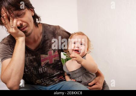 Das Kind schreit hysterisch. Ein müder Vater will das Baby nicht hören. Der Elternteil ist irritiert, müde, will eine Pause von seiner Tochter machen Stockfoto