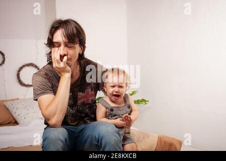 Das Kind schreit hysterisch. Ein müder Vater will das Baby nicht hören. Der Elternteil ist irritiert, müde, will eine Pause von seiner Tochter machen Stockfoto