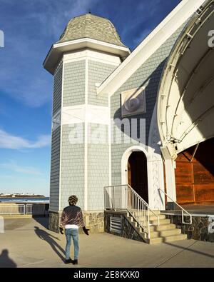 Person in lila Jacke und Jeans gekleidet stehen mit offenen Armen vor der Seashell Bühne, als die Sonne an einem Wintertag untergeht. Stockfoto