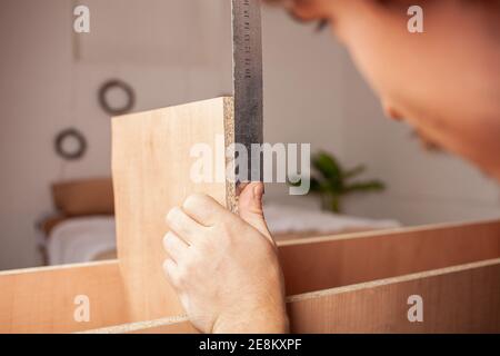 Ein Mann misst ein Linealregal für ein Kabinett aus Holzspänen. Stockfoto