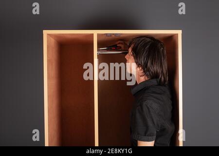 Ein Mann dreht ein Rohr für einen Aufhänger in einem Schrank mit einem Schraubendreher. Die Querlatte zum Aufhängen der Kleidung. Stockfoto