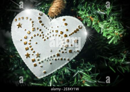 Extreme Nahaufnahme eines weißen und goldenen Herzens, das an einem Weihnachtsbaum hängt. Stockfoto